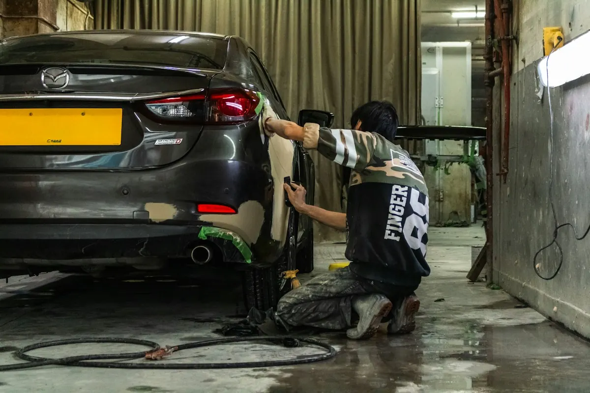 Auto body technician sanding a car's rear panel before paint